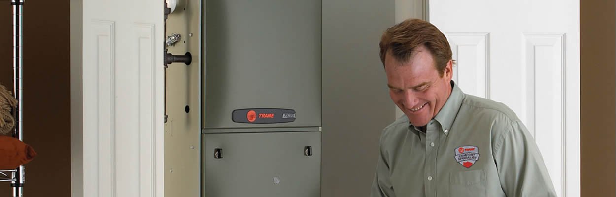 Hvac Technician Standing Next To Trane Furnace Writing On Clipboard